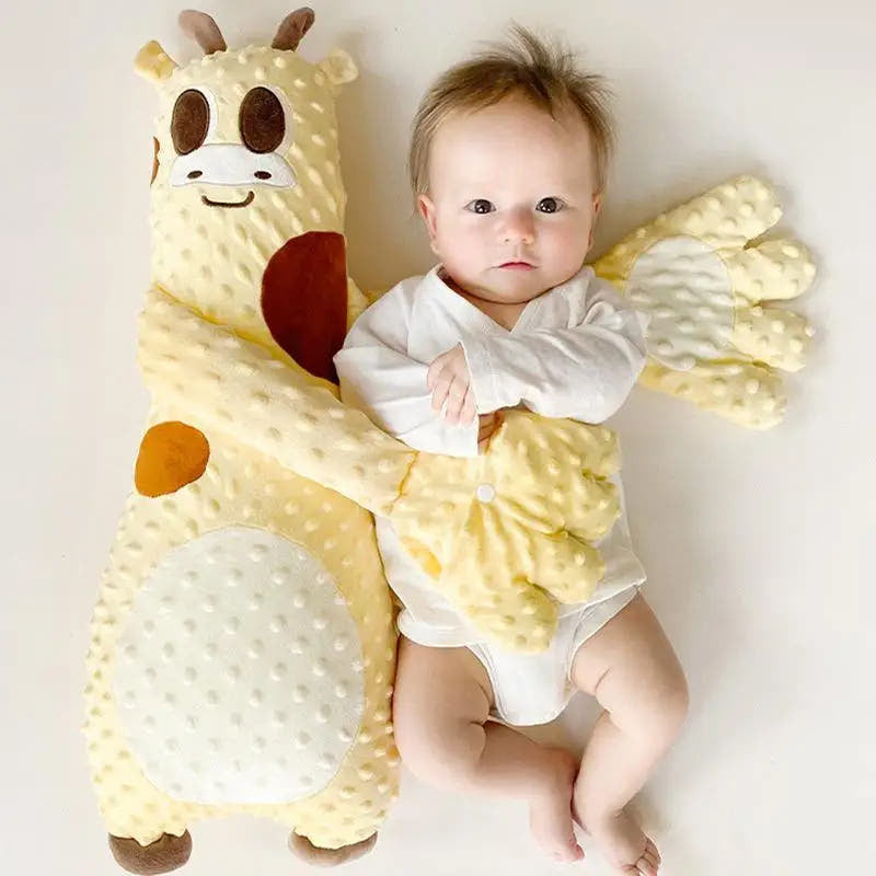 Baby lying next to a soft toy shaped like a giraffe on a plain background