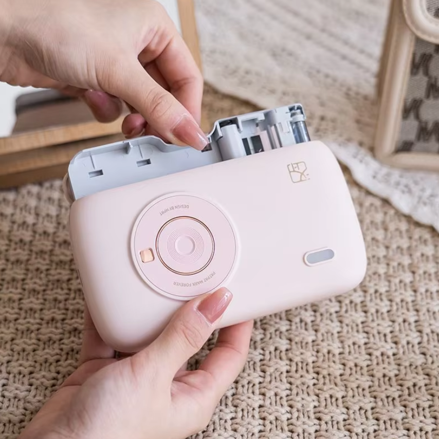 Pink instant camera being held with a hand on a textured surface