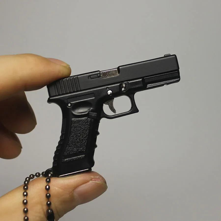 Black gun-shaped keychain held by a hand against a gray background