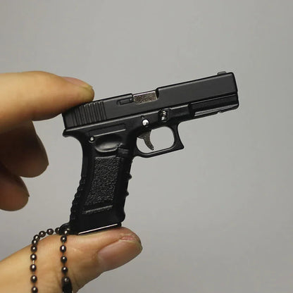 Black gun-shaped keychain held by a hand against a gray background